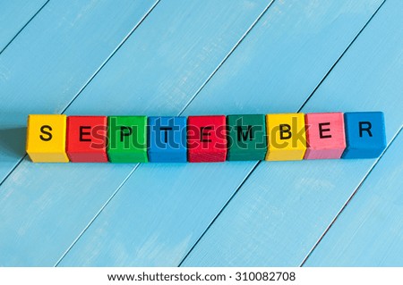 Word September - one of autumn month on colorful wooden cubes with light wood background.