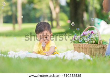 Asia Baby boy sitting on green grass in the park with soap bubbles