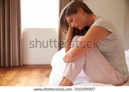 Woman Suffering From Depression Sitting On Bed In Pajamas Royalty-Free Stock Photo #310309007