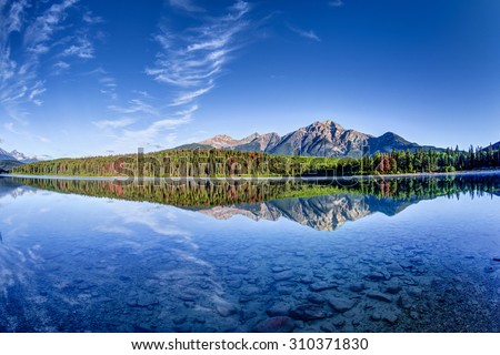 Colorful trees lined the shores of Patricia Lake at Jasper National Park with Pyramid Mountain in the background. The calm lake reflects a mirror image of the mountains and trees. Royalty-Free Stock Photo #310371830