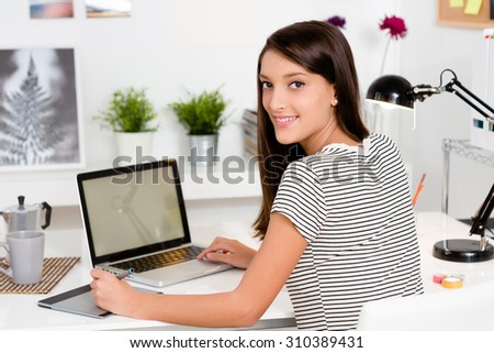 Portrait of young woman working with laptop in her workspace. View from behind