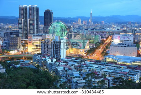 Aerial panorama of vibrant Taipei City, the capital of Taiwan, with view of a giant Ferris wheel in Dazhi Commercial District & Taipei 101 Tower among skyscrapers in downtown area under blue twilight