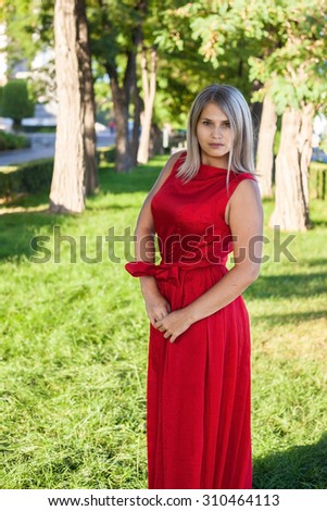 beautiful girl posing in a red evening dress in the park outdoors