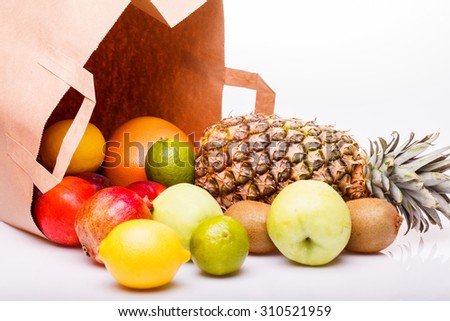 Fresh tropical fruits of pineapple orange juicy grapefruit yellow lemon ripe nectarine purple plum red pomegranate kiwi lime and green apple and paper pack on white background, horizontal picture