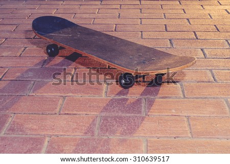 Vintage skateboard is standing on paved footpath backlit by sunset. We can see long shadows on surface. Warm light. A lot of place for text.