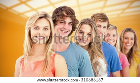 A smiling group standing behind each other against white room with windows at ceiling
