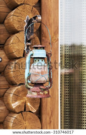 Old retro kerosene lantern hanging on the wall of the log house as a background for creative design.