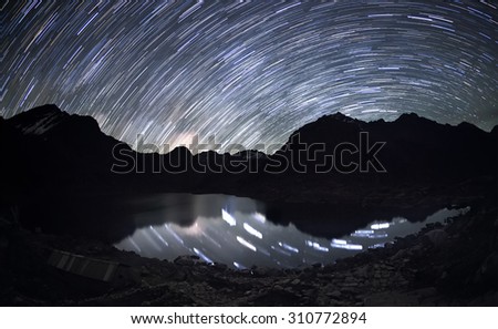 Star trails over the mountains and the reflection of the stars in a water beneath them. 