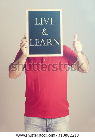 Man holding a blackboard with Live and Learn message. Cross processed image for retro look