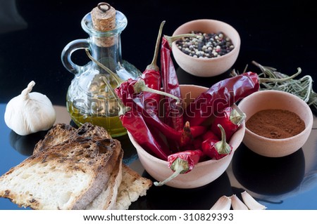 red chillies, oil, bread, garlic and pepper in a jar of clay on a black background