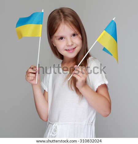 Beautiful cheerful little girl in a white dress holding a flag of Ukraine on Independence Day