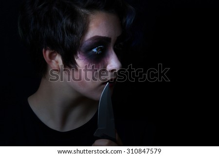 Teen girl masked in scary makeup with combat knife on black background. 