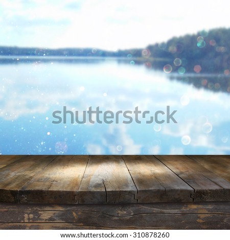 vintage wooden board table in front of dreamy and abstract forest lake landscape with lens flare and glitter overlay

