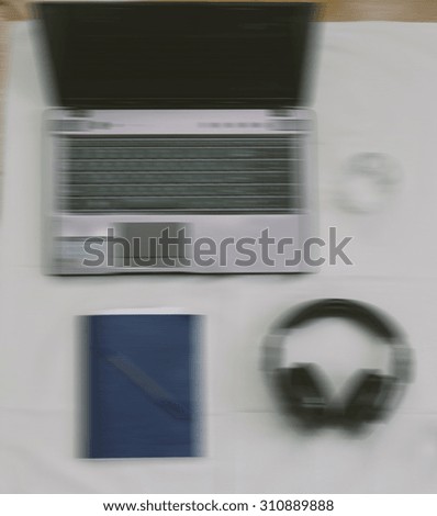 Motion blurred effect on the photo with workplace with open laptop, business documents, headphones, workbook and pen.