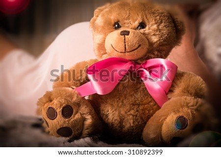 Teddy bear plush toy with pink bow is sitting next to pregnant woman
Picture edited with creative lighting, flares and vignetting added to emphasize abstract concept