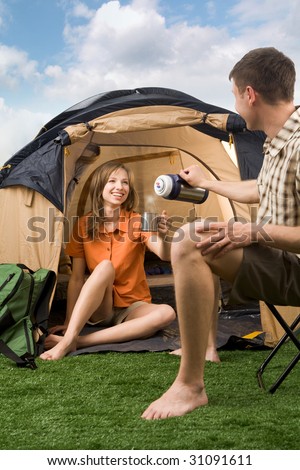 Photo of cheerful girl and guy lying on green grass in tent and looking at camera with smiles