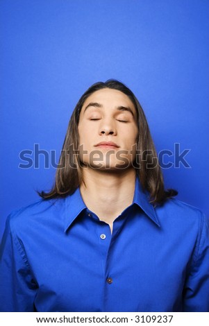 Portrait of Asian-American teen boy with eyes closed against blue background.