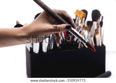 Set of many professional make-up brushes for eyeshadow powder and facial foundation for visagistes in black plastic box and human hand holding one brush on white background, horizontal picture