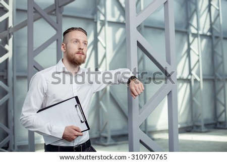 Attractive businessman has a meeting with his business partner. He is standing and leaning on the construction. The man is looking forward in anticipation and with hope. Copy space in right side