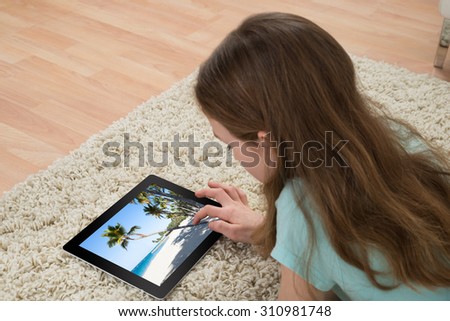 Girl Lying On Carpet Looking At Photo On Digital Tablet