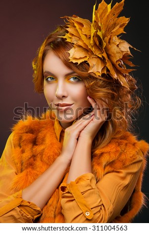 Beautiful young woman in orange, yellow make-up and clothes with autumn leaves in her red curly hair