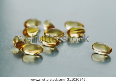 Yellow capsule with vitamin E tocopherol on blue surface, selective focus Royalty-Free Stock Photo #311020343