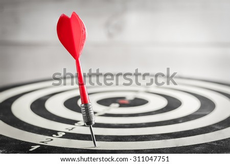 Red dart arrow missed in the target center of dartboard