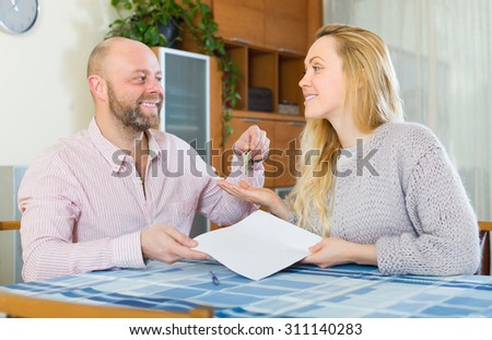 Smiling agent giving to positive female client keys from flat and papers