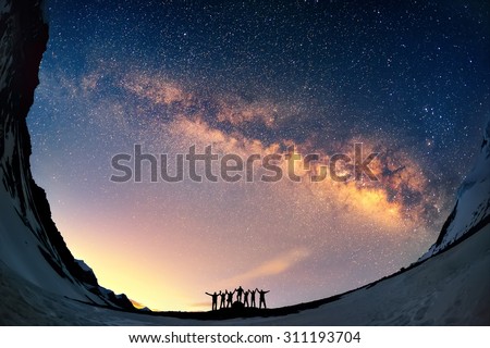 Teamwork and support. A group of people are standing together holding hands against the Milky Way in the mountains. 