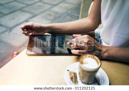 Cropped image with woman's hands touching screen of digital tablet at the table with cup of coffee