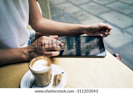 Cropped image with female hands touching screen of digital tablet at the coffee shop table               