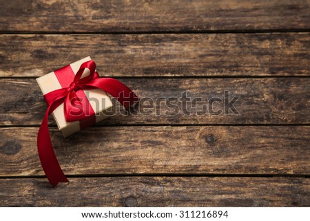 One gift box with an red big ribbon on old wooden dark brown background for christmas.