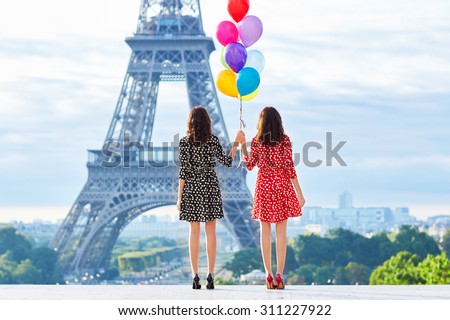 Beautiful twin sisters in red and black polka dot dresses with huge bunch of colorful balloons in front of the Eiffel tower in Paris, France Royalty-Free Stock Photo #311227922