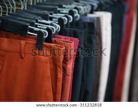 colorful trousers shop ,,through new clothes during shopping,Colorful man and woman's dresses on wood hangers in a retail shop. Fashion and shopping business concept.red jeans background.
