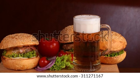 Few fresh tasty burgers of green lettuce meat cutlet tomato and white bun with sesame seeds near and glass of light beer with froth on octoberfest holiday closeup, horizontal picture