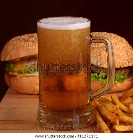 Two fresh tasty burgers of green lettuce meat cutlet cheese tomato and white bread bun with sesame seeds near chips and glass of light beer on octoberfest holiday, square picture