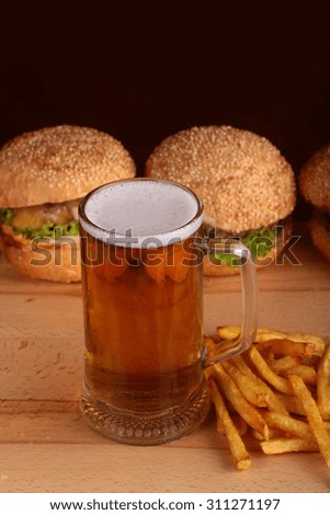 Two fresh tasty burgers of green lettuce meat cutlet cheese tomato and white bread bun with sesame seeds near chips and glass of light beer on octoberfest holiday, vertical picture