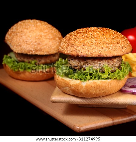 Big tasty appetizing fresh burgers of green lettuce red tomato cheese and bacon slice meat cutlet and white bread bun with sesame seeds chips and violet onion closeup, square picture