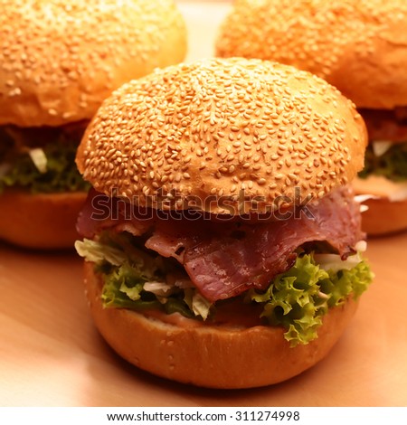 Few big tasty appetizing fresh burgers of green lettuce red tomato cheese and bacon slice and white bread bun with sesame seeds closeup, square picture