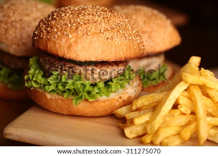 Big tasty appetizing fresh burgers of green lettuce red tomato cheese and bacon slice meat cutlet and white bread bun with sesame seeds and chips closeup, horizontal picture