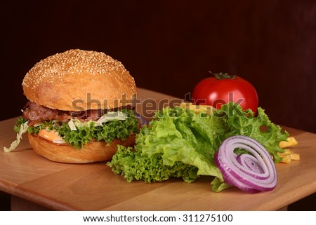 One big tasty appetizing fresh burger of green lettuce red tomato cheese bacon slice meat cutlet violet oinion and white bread bun with sesame seeds on black background closeup, horizontal picture