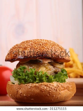 One big delicious fresh burger of green lettuce red tomato cheese meat cutlet violet oinion and white bread bun with sesame seeds on wooden background closeup, horizontal picture