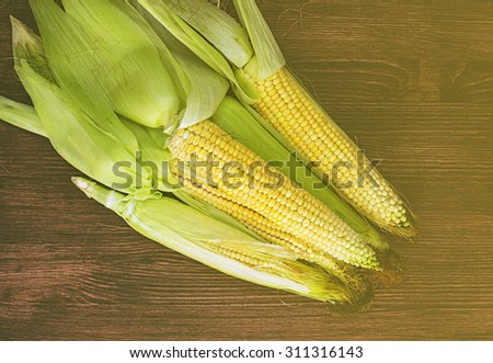 Ripe corn with green leaves on the wooden brown table, toned picture