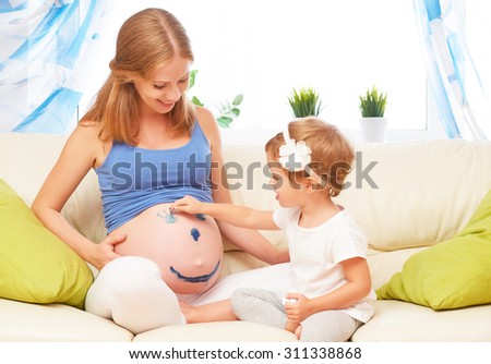 happy family in anticipation of the baby. Pregnant mother and child daughter paint colors on the tummy