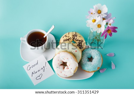 Four donuts on saucer with cup of tea. Aquamarine background