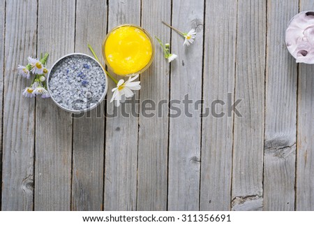 yellow calendula cream in glass pot, moisturizer and bath salt with white herbal flowers on weathered rusty wooden table background