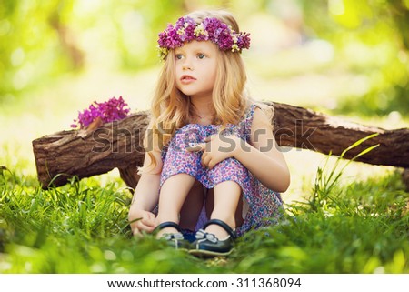 Portrait of cute blond girl dressed wreath of lilac on a head in green field