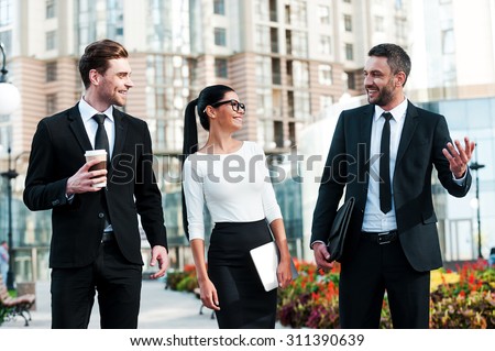 Quick briefing before meeting. Three cheerful young business people talking to each other while walking outdoors Royalty-Free Stock Photo #311390639