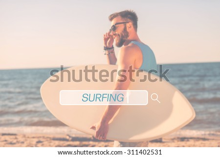 Find your place for surfing. Handsome young man holding skimboard and adjusting eyewear while walking along the beach 