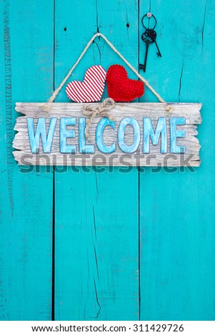 Rustic wood welcome sign with red fabric hearts and black iron skeleton keys hanging on teal blue antique wooden background